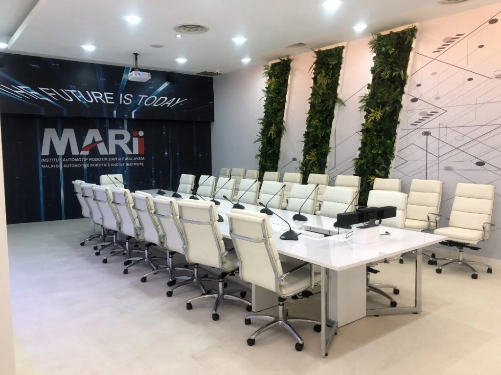 A modern conference room showcases sleek interior design with white chairs around a table, a green plant wall decor, designed by Moonman Events sdn bhd for Malaysia Automotive Robotics and IoT Institute (Marii)