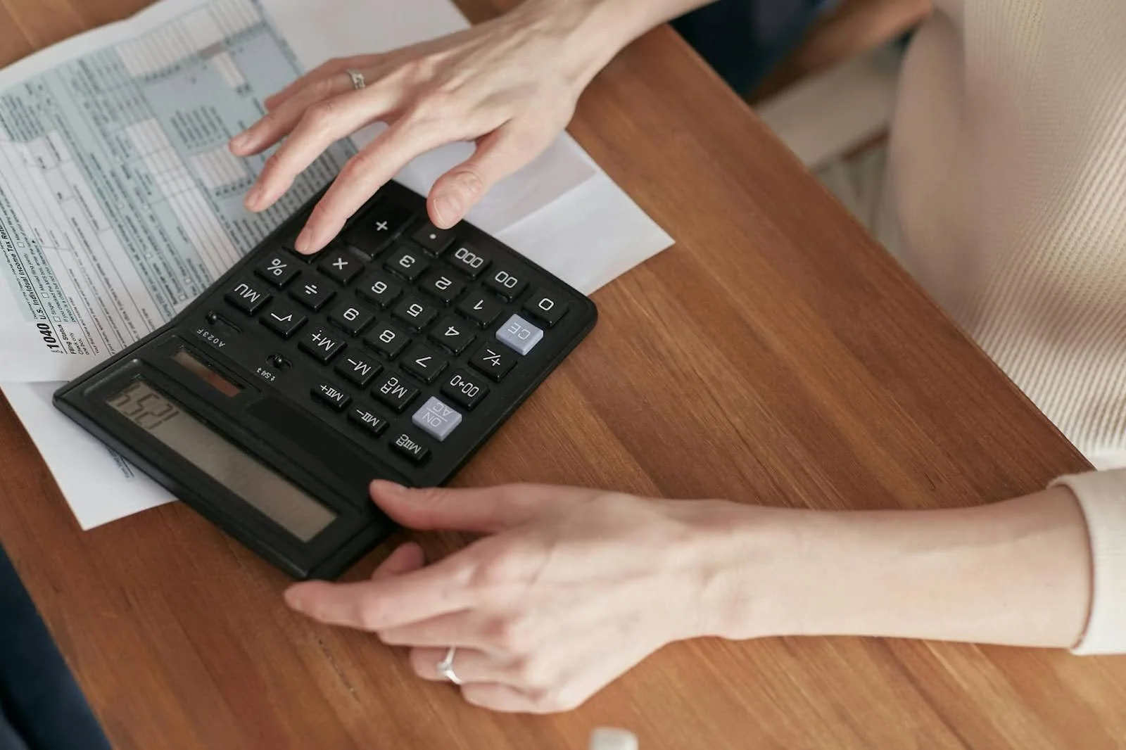 a shot of a person's hands using a calculator with a paper behind it