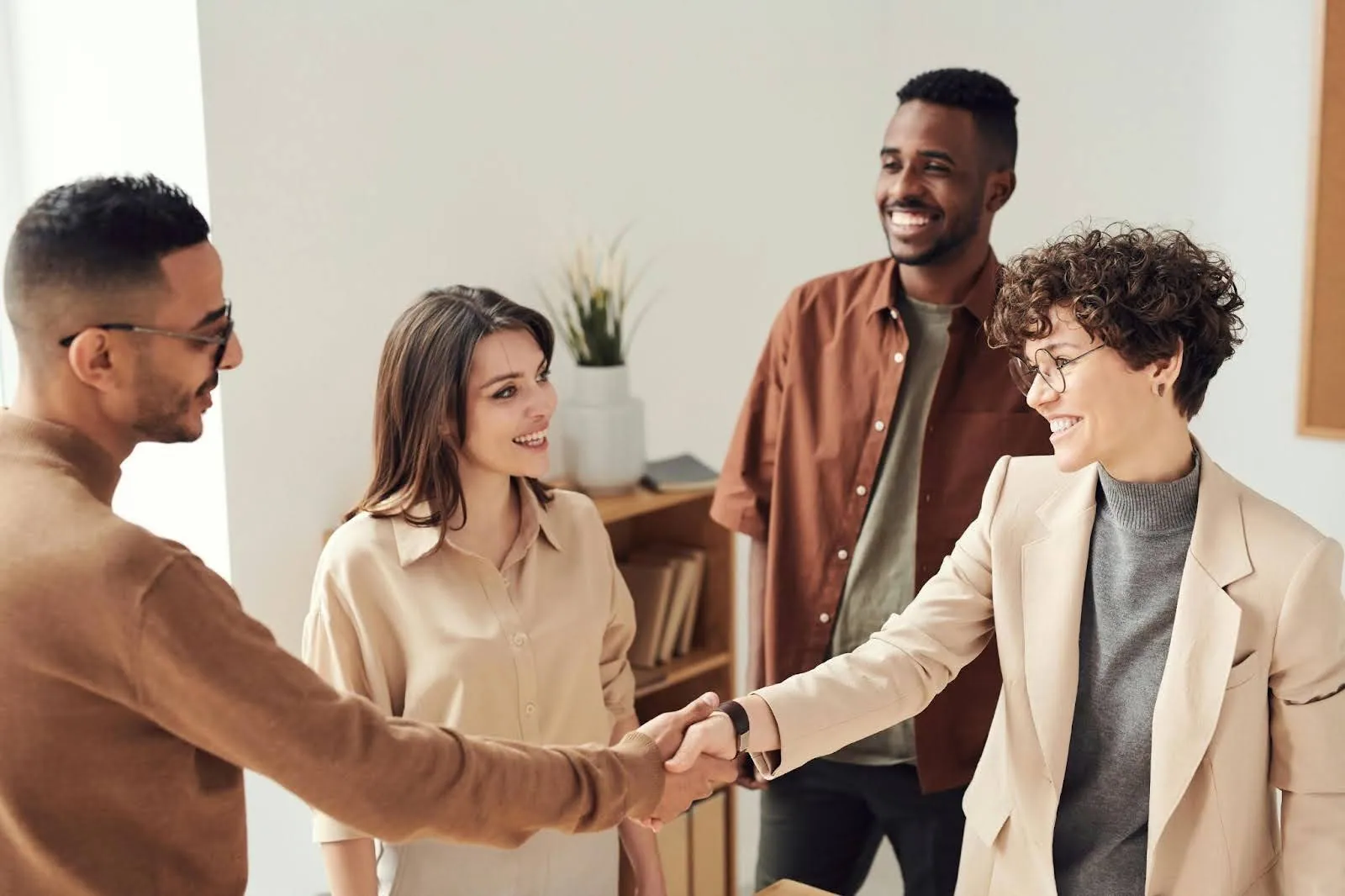 a group of people smiling while a man and a woman shaking hands in a business setting