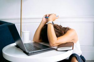 a woman puts her face on the table in front of a laptop with a notebook under her left arm stressing out from finding the best event company in malaysia